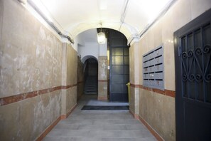 Ein Flur mit Fliesenboden, einer Tür mit einem Metallgitter und einer Treppe im Hintergrund.