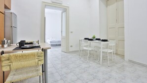 Uma cozinha compacta com geladeira, uma área de refeições com mesa e cadeiras, e uma porta branca que dá para outro cômodo.