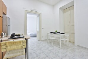 A compact kitchen with a refrigerator, a dining area with a table and chairs, and a white door leading to another room. - A comfortable and large apartment ideal for four guests and strategically located in the heart of Naples, allowing you to fully experience the city's authentic atmosphere; it is just steps away from Piazza del Plebiscito and the entrance to the evocative (Napoli)