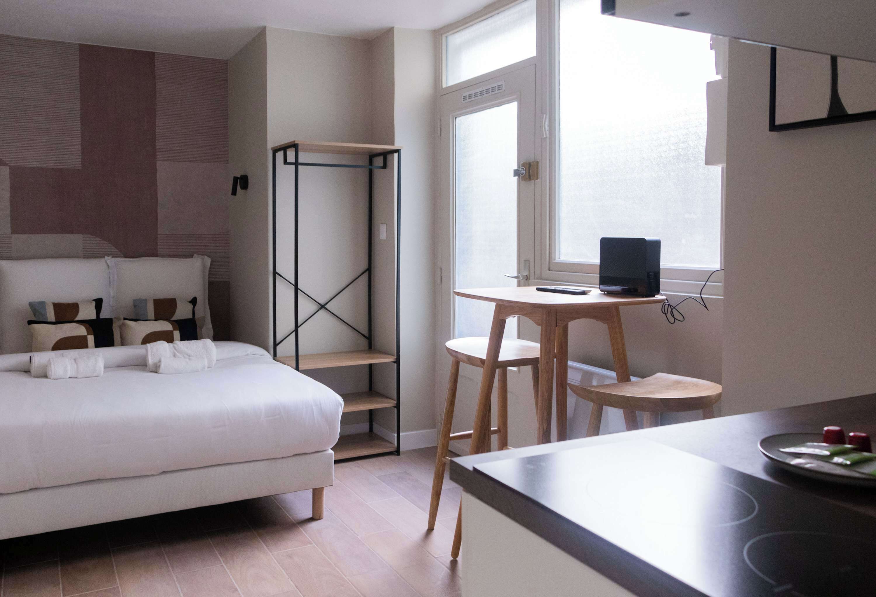 A hotel room with a bed, a desk with a chair, a wardrobe, and a window.