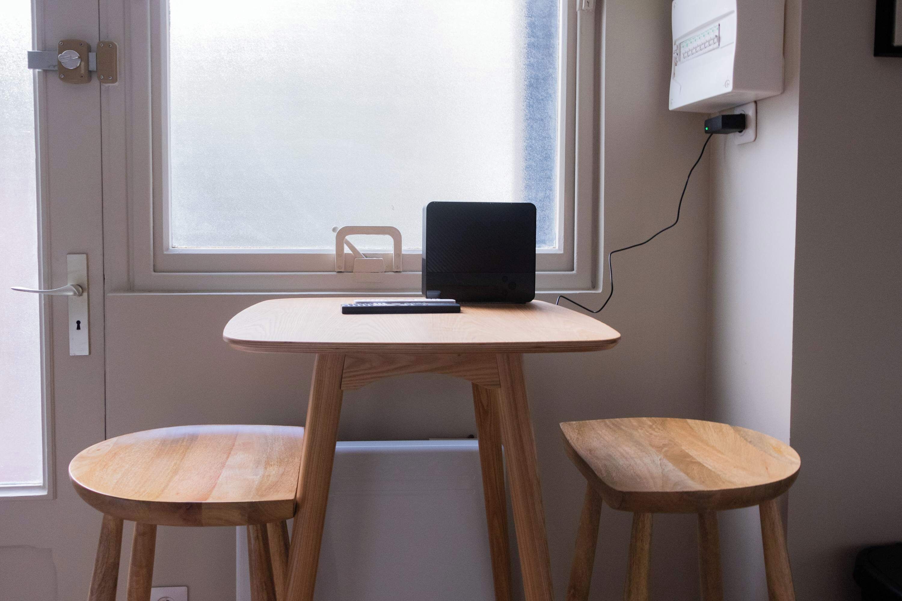 A small wooden table with a laptop and a remote control on it, positioned in front of a window with a view of the outside.