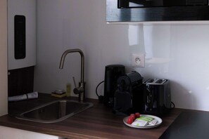 A compact kitchen with a sink, a coffee maker, a toaster, and a plate with food items. - Studio parisien cosy, proche Opéra/Saint-Lazare (Paris)