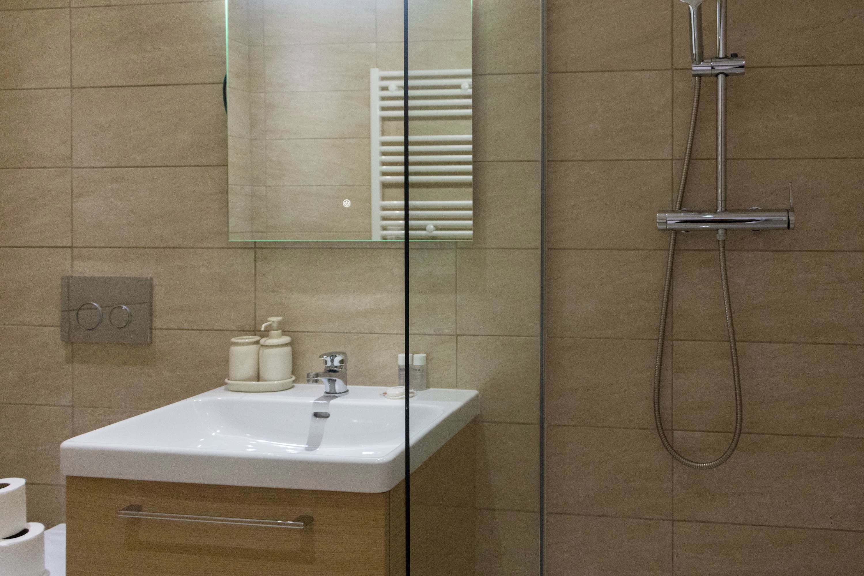A bathroom with a white sink, a mirror, a shower, and a towel rack.