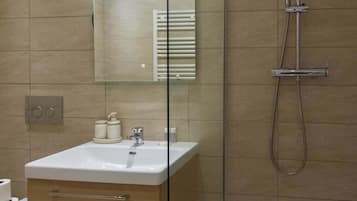 A bathroom with a white sink, a mirror, a shower, and a towel rack.