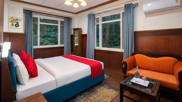 A hotel room with a bed, a sofa, a mirror, and a window with curtains. - Shimla PineCrest Retreate (Shimla)