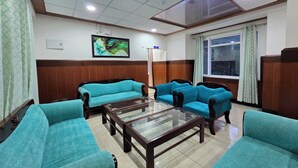 A room with teal sofas, a glass coffee table, a painting on the wall, and a window with curtains. - Shimla PineCrest Retreate (Shimla)