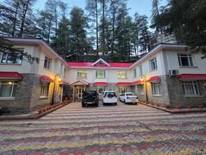 A building with a red roof, multiple windows, and a paved entrance with parked cars.