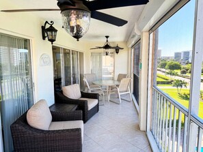 A balcony with wicker furniture, a ceiling fan, and a view of a park and buildings. - Oceanside Marco Island Retreat: Expansive Views of Sunset, Pool & Beach (Marco Island)