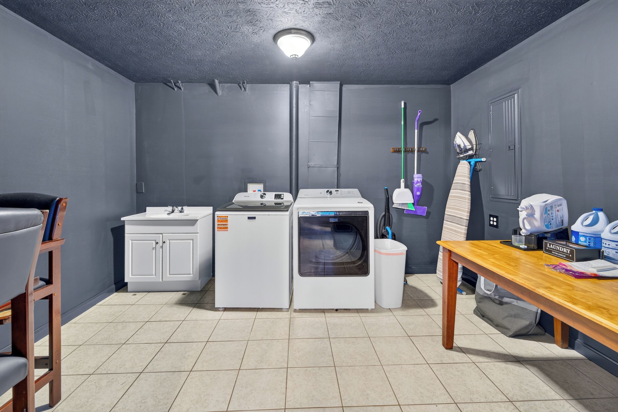 A laundry room with a washing machine, dryer, sink, and a table with cleaning supplies.