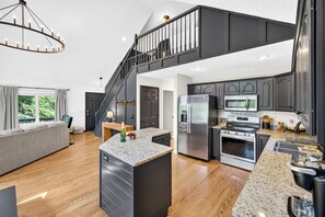 A modern kitchen with a central island, stainless steel appliances, and a staircase leading to an upper level.