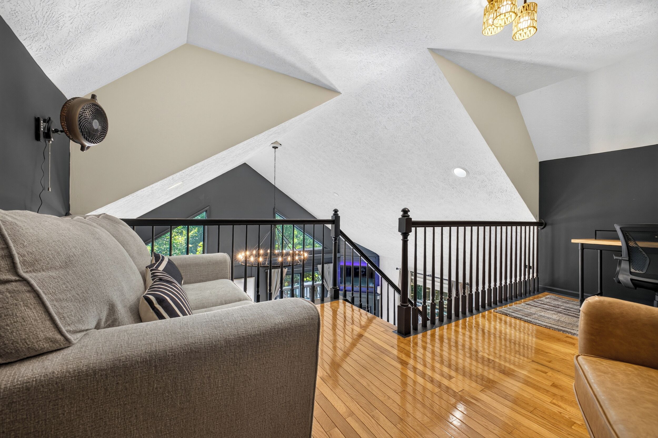 Un moderno spazio abitativo in stile loft con soffitto alto, pavimento in legno, un divano, una scrivania e una scala che conduce a un livello superiore.