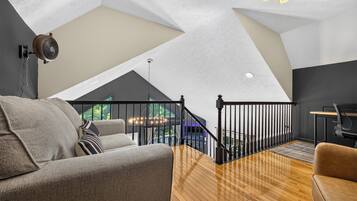 Un moderno spazio abitativo in stile loft con soffitto alto, pavimento in legno, un divano, una scrivania e una scala che conduce a un livello superiore.