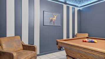 A pool table with balls, a sofa, and a framed deer picture in a room with vertical paneling and a ceiling with lights.