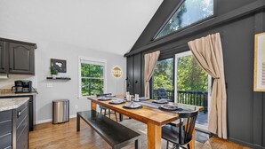 Een eetruimte met een houten tafel voor vier personen, een bank en uitzicht op een balkon met gordijnen.
