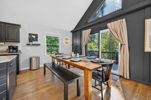 Un comedor con una mesa de madera preparada para cuatro, un banco y vistas a un balcón con cortinas.