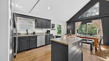 A modern kitchen with dark cabinetry, a central island, and a dining area with a view of greenery.