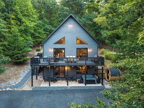 A two-story cabin with a balcony, outdoor seating, and a hot tub.