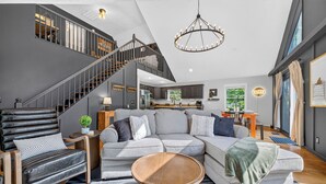 Een moderne woonkamer met een grijze bank, een houten salontafel en een trap naar een hoger gelegen verdieping.