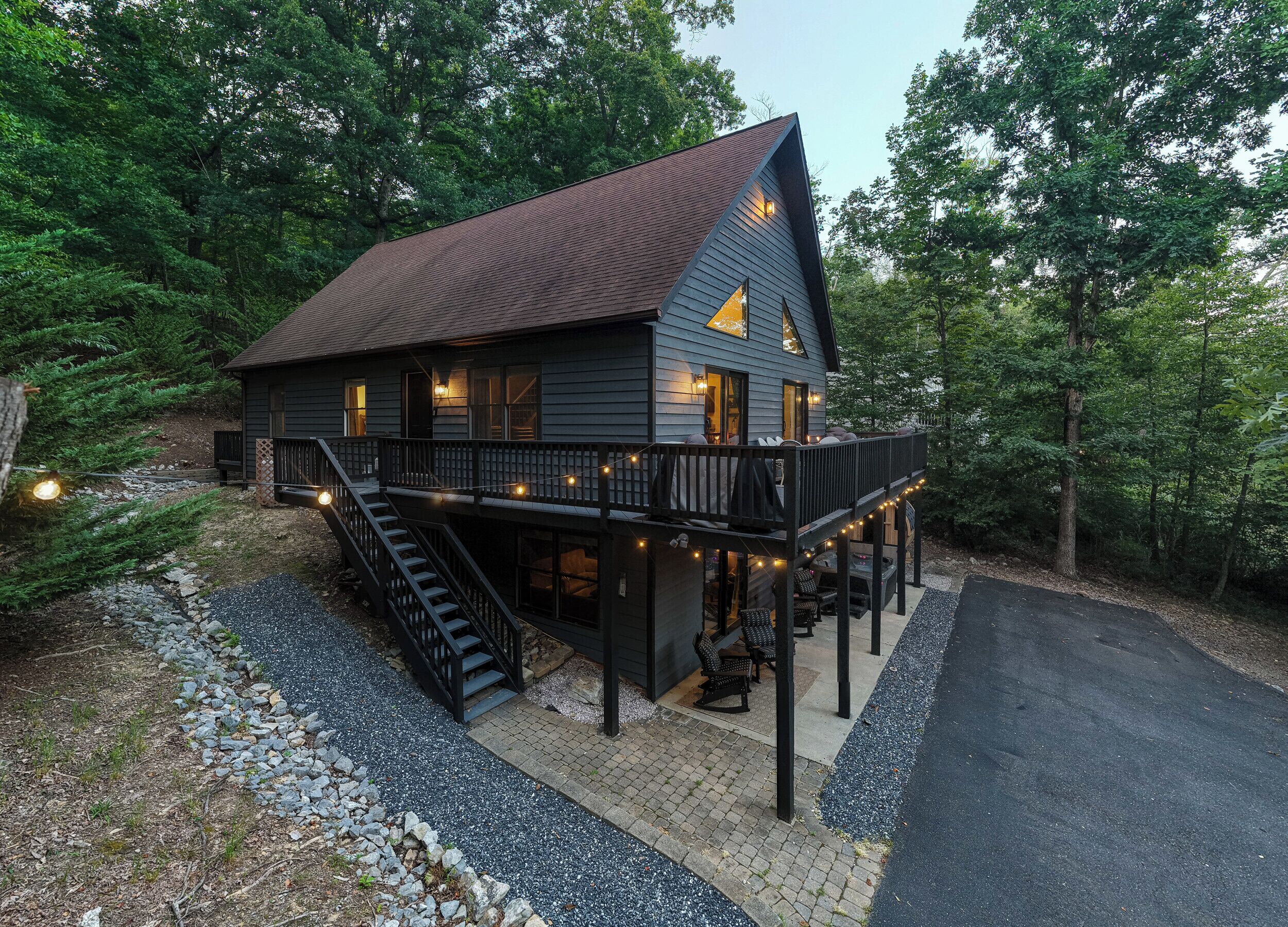 A two-story cabin with a balcony, a staircase, and a driveway.