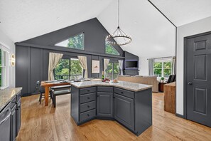 A modern kitchen with dark cabinetry, a large island, and a dining area with a view of the outdoors.