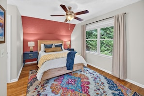 A bedroom with a bed, a ceiling fan, a nightstand, a window with curtains, and a rug.