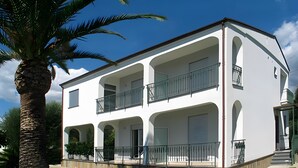 A two-story building with a balcony on the upper floor, a palm tree in the foreground, and a well-maintained lawn. - Apartment 'Comics' with sea view, Wi-Fi and air conditioning (Villammare)