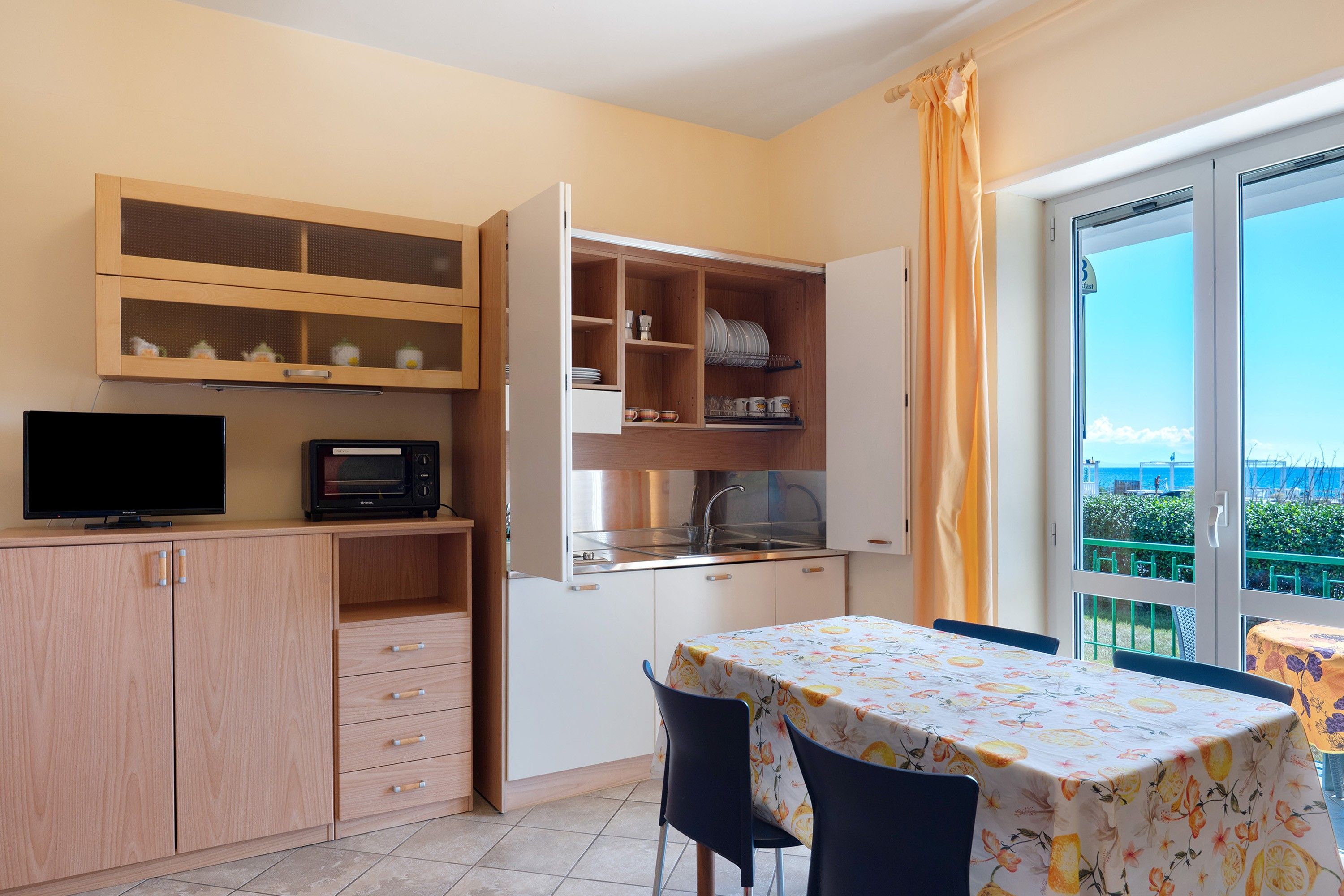 Une cuisine compacte équipée d’une télévision, d’un four à micro-ondes et de placards. On y trouve également un coin repas avec une table et des chaises, et une vue par la fenêtre.