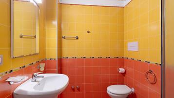 Un baño con azulejos amarillos y anaranjados, un lavamanos blanco, un inodoro y un espejo.