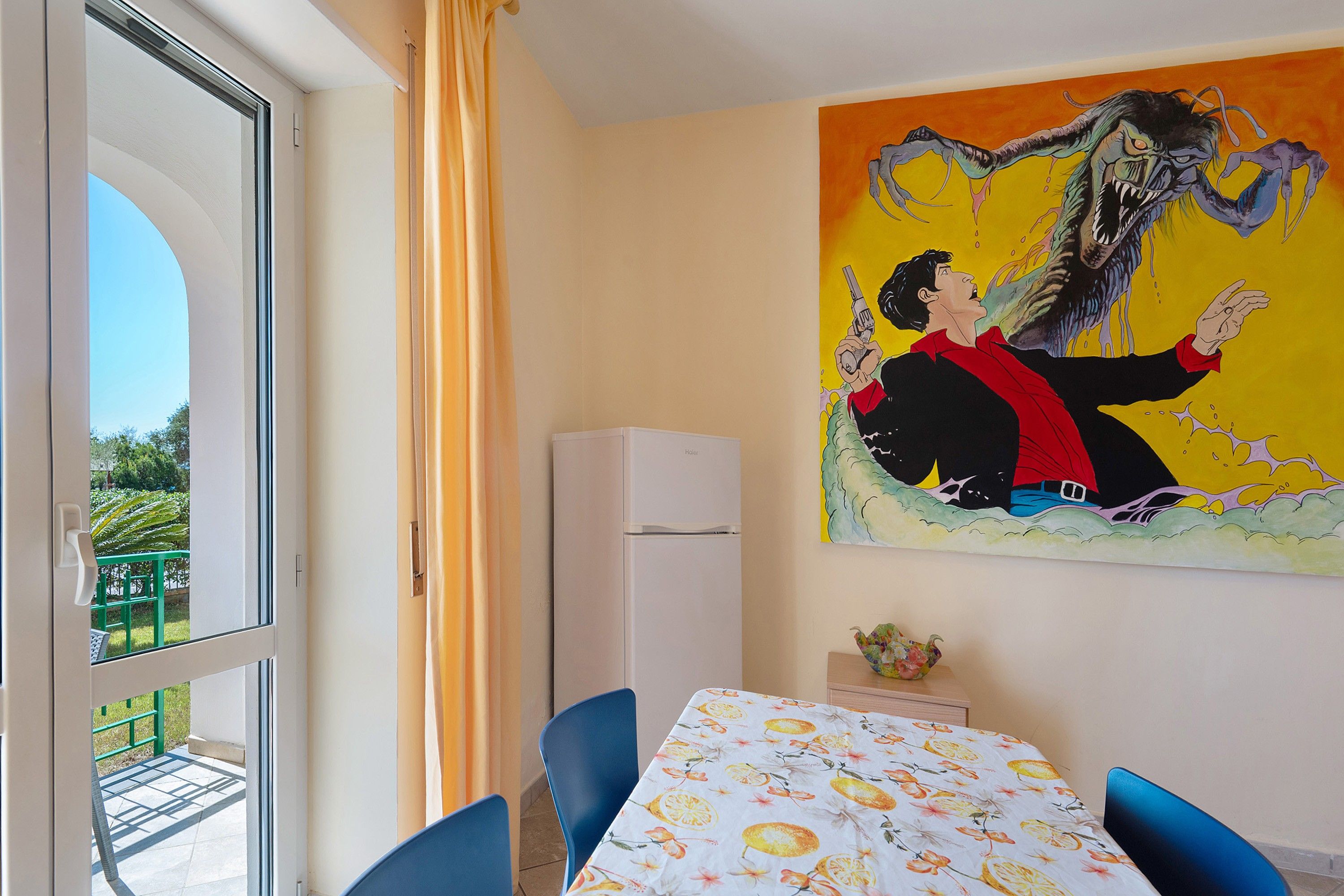 A room with a dining table, chairs, a painting, and a view through a glass door.