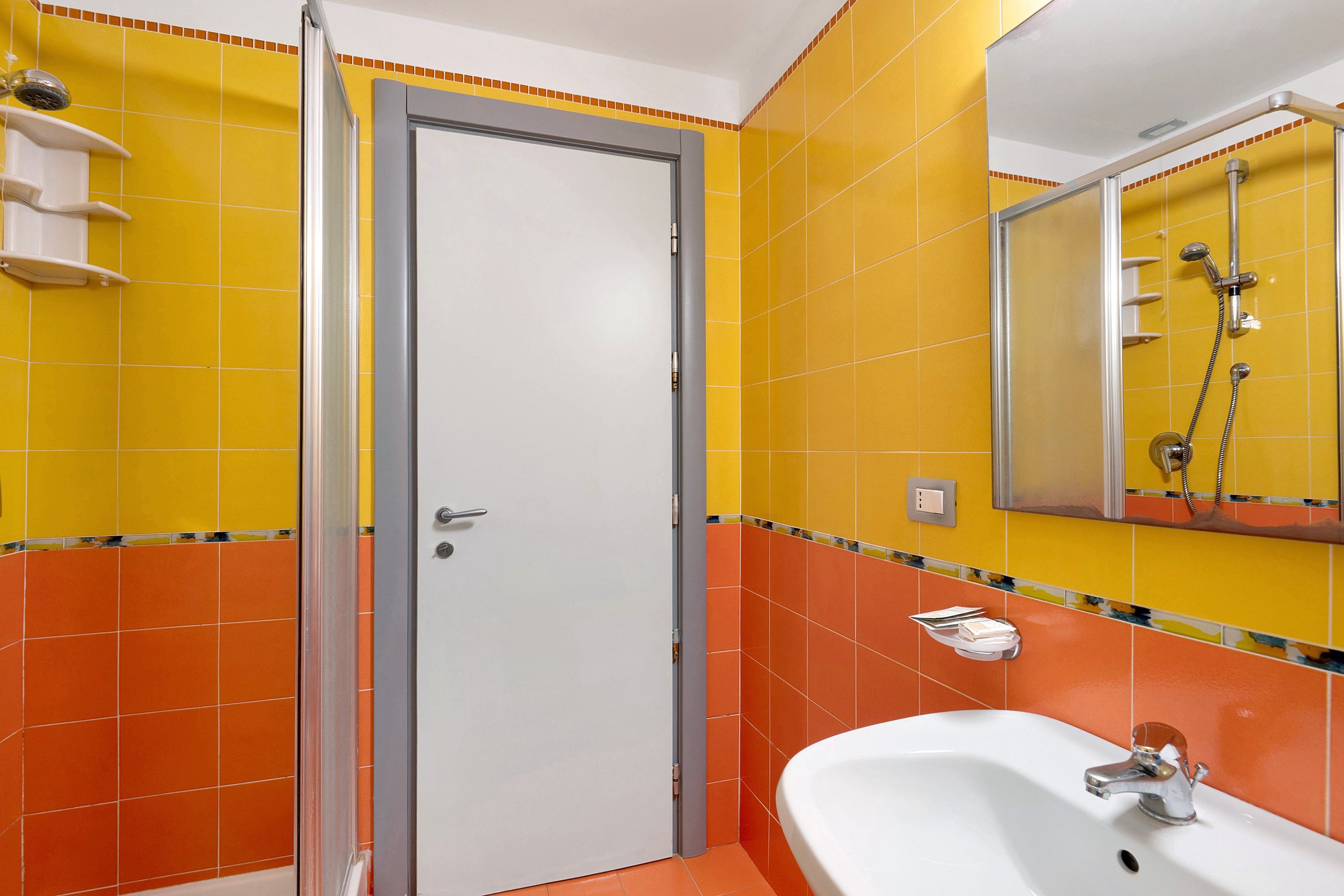 Ein Badezimmer mit einem weißen Waschbecken, einer Dusche und einer Tür mit Griff.