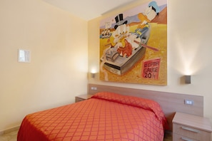 Una habitación de hotel con una cama, una mesita de noche, una lámpara de pared y un cartel grande en la pared.
