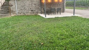 Un edificio de piedra con techo de tejas, un área de estar al aire libre cubierta con sillas y una mesa, y un césped.