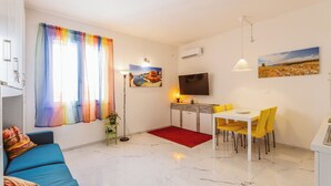 A modern living room with a blue sofa, a dining area with yellow chairs, a red rug, and a painting on the wall.