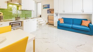 A modern kitchen with a white countertop, a yellow chair, and a blue sofa with orange pillows.