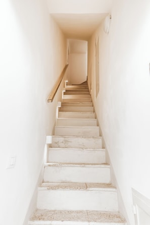 A staircase with white walls and a wooden handrail leading to a door at the top.