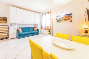 A modern kitchen with white cabinets, a blue sofa, and a dining table with yellow chairs.