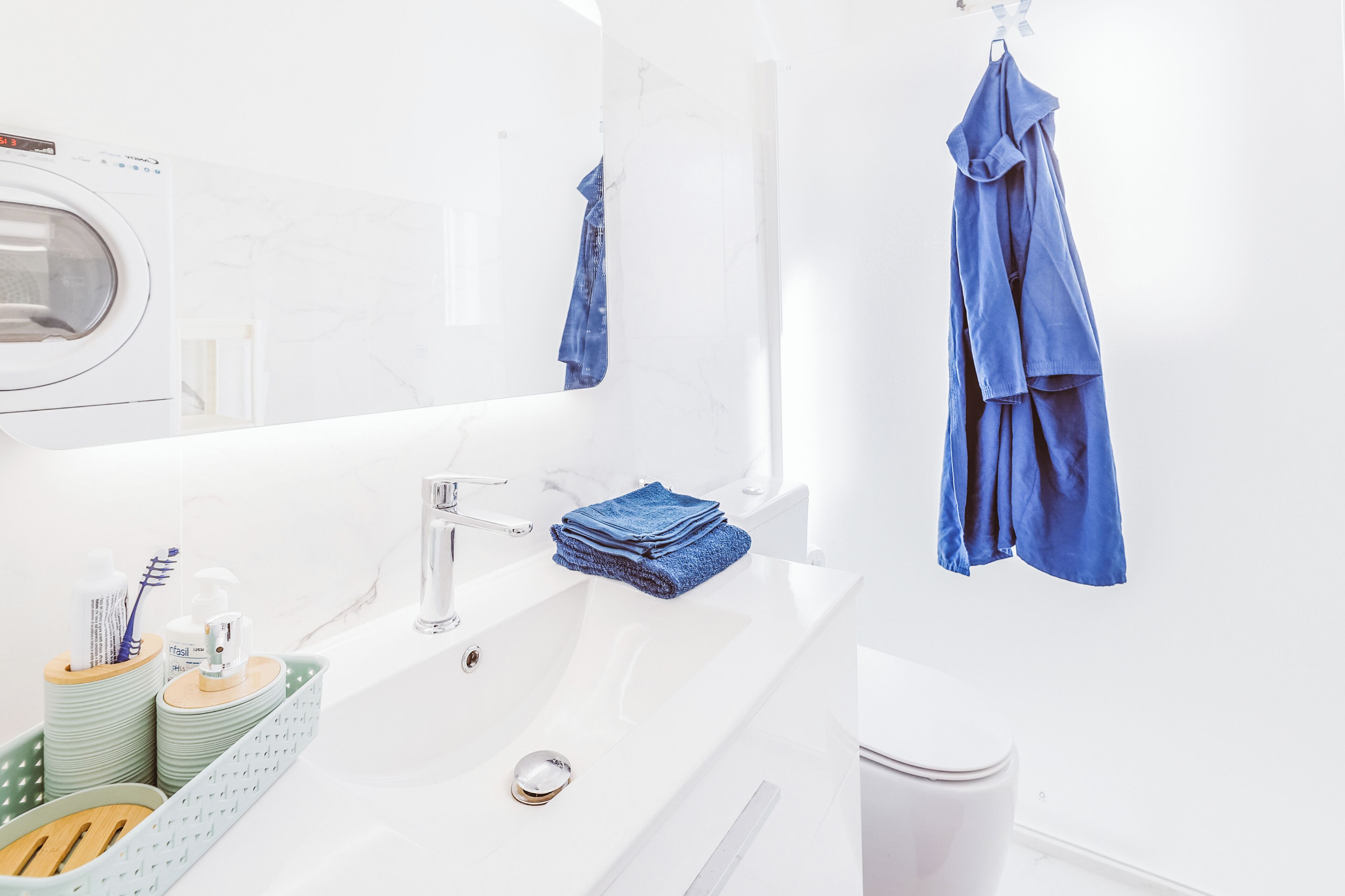 Ein modernes Badezimmer mit einem weißen Waschbecken, einem Spiegel und einem blauen Handtuch an der Wand.