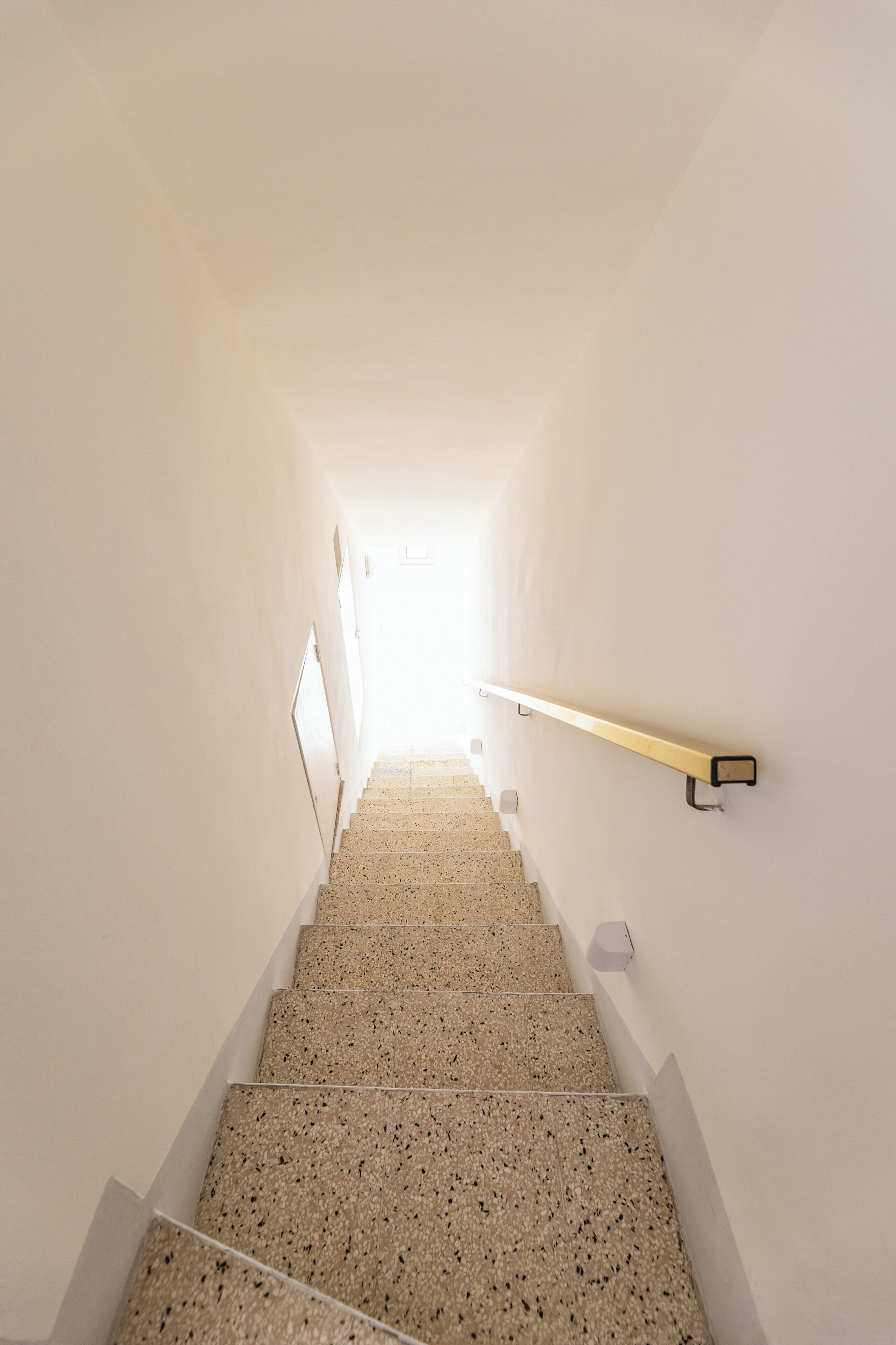 A staircase with a handrail on the right, leading to a bright area at the top.