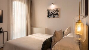 Una habitación de hotel con cama, mesita de noche, lámpara y una obra de arte en la pared.