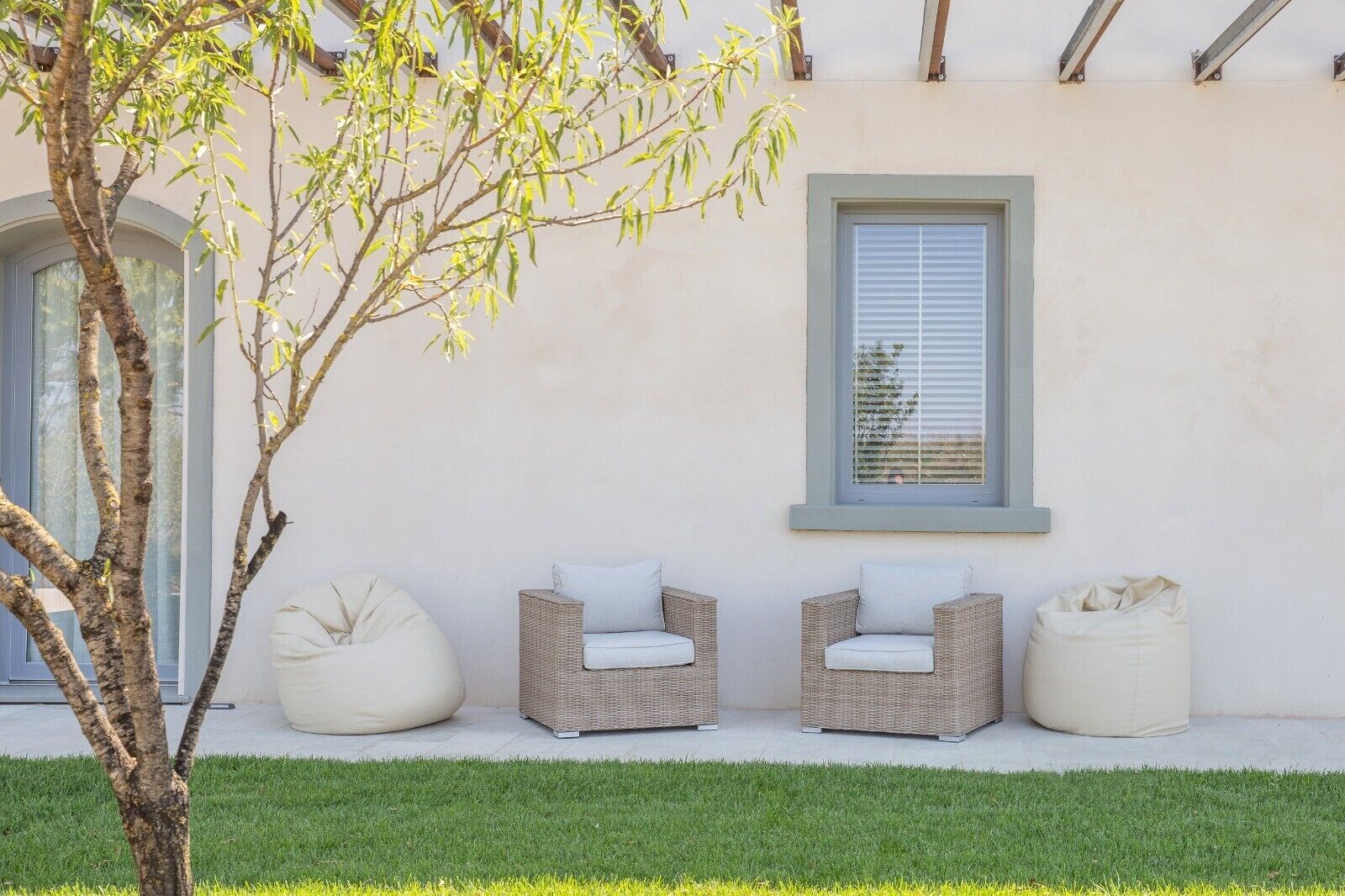 A building exterior with a window, two wicker chairs with cushions, and a tree.