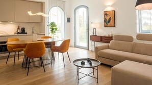 Una sala de estar moderna con un sofá, una mesa de comedor con sillas y una zona de cocina con armarios y una ventana.