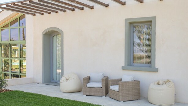 Un patio con mobiliario de mimbre, un sillón de peluche y una puerta de vidrio.