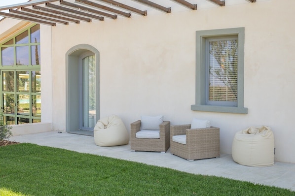 Un patio con mobiliario de mimbre, un sillón de peluche y una puerta de vidrio.