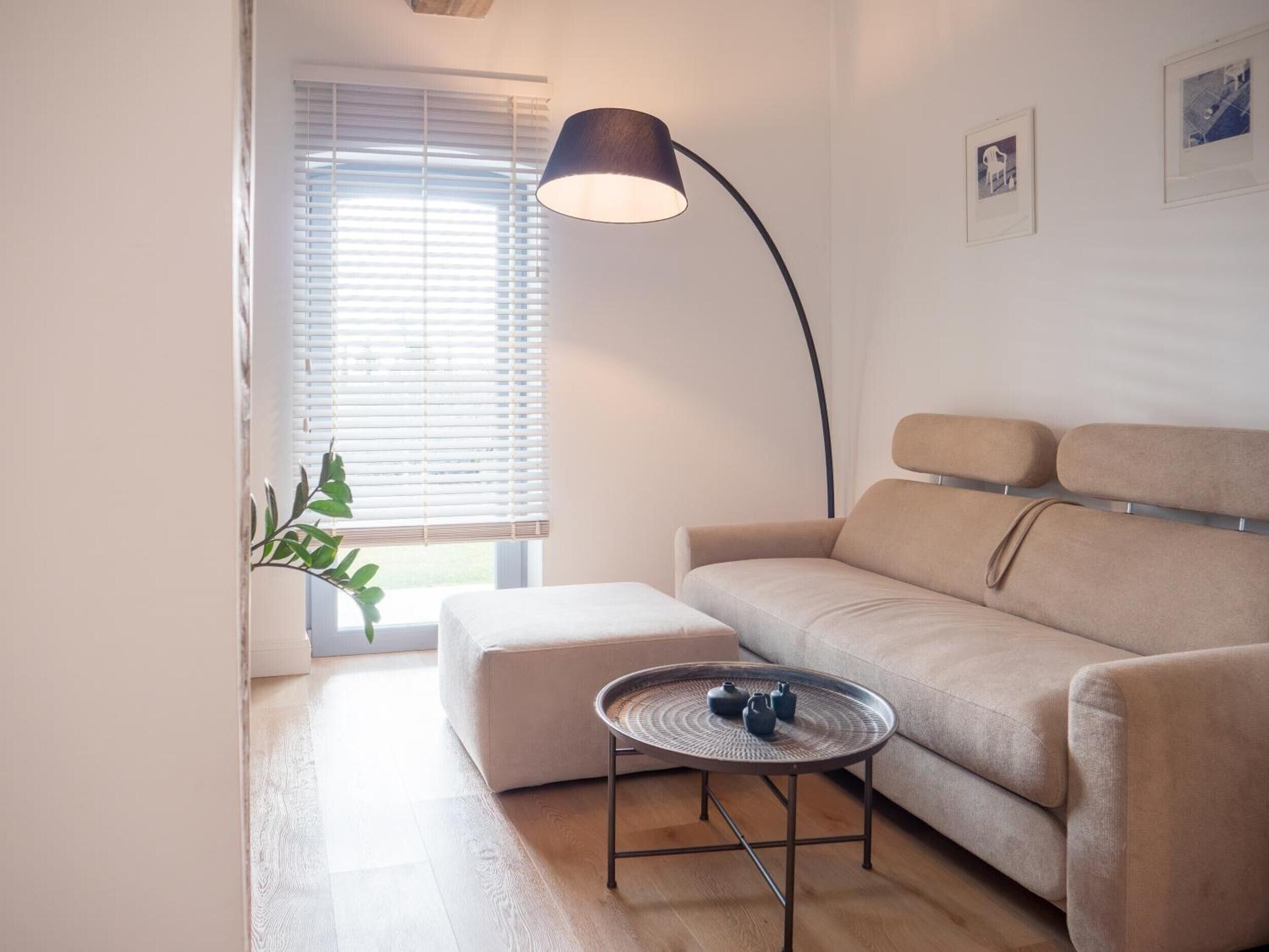 Ein modernes Wohnzimmer mit einer Couch, einem runden Couchtisch, einer Stehlampe und einem Fenster mit Jalousien.
