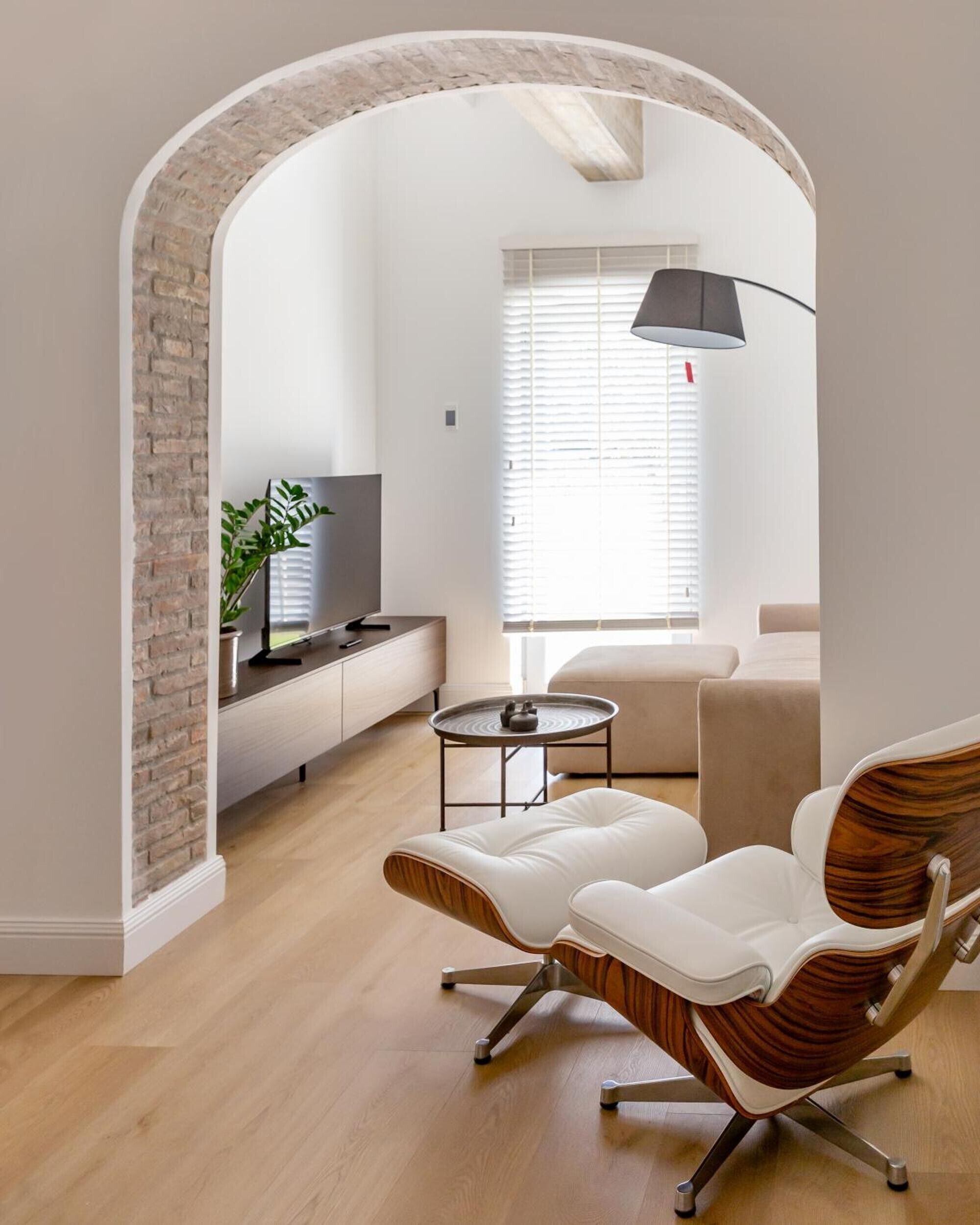 Un salon moderne avec un mur en briques, un téléviseur à écran plat, une table basse et deux fauteuils en cuir blanc.