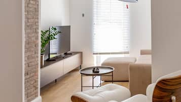 Un salon moderne avec un mur en briques, un téléviseur à écran plat, une table basse et deux fauteuils en cuir blanc.