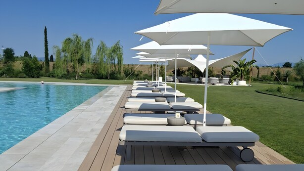 A poolside area with lounge chairs and umbrellas, a clear sky, and a view of the landscape.