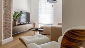 A modern living room with a brick accent wall, a flat-screen TV, a potted plant, a round coffee table, and a sofa.