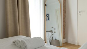 A hotel room with a bed, a rolled white towel, a mirror, and a door.