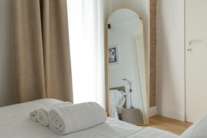 Una habitación de hotel con cama, una toalla blanca enrollada, un espejo y una puerta.